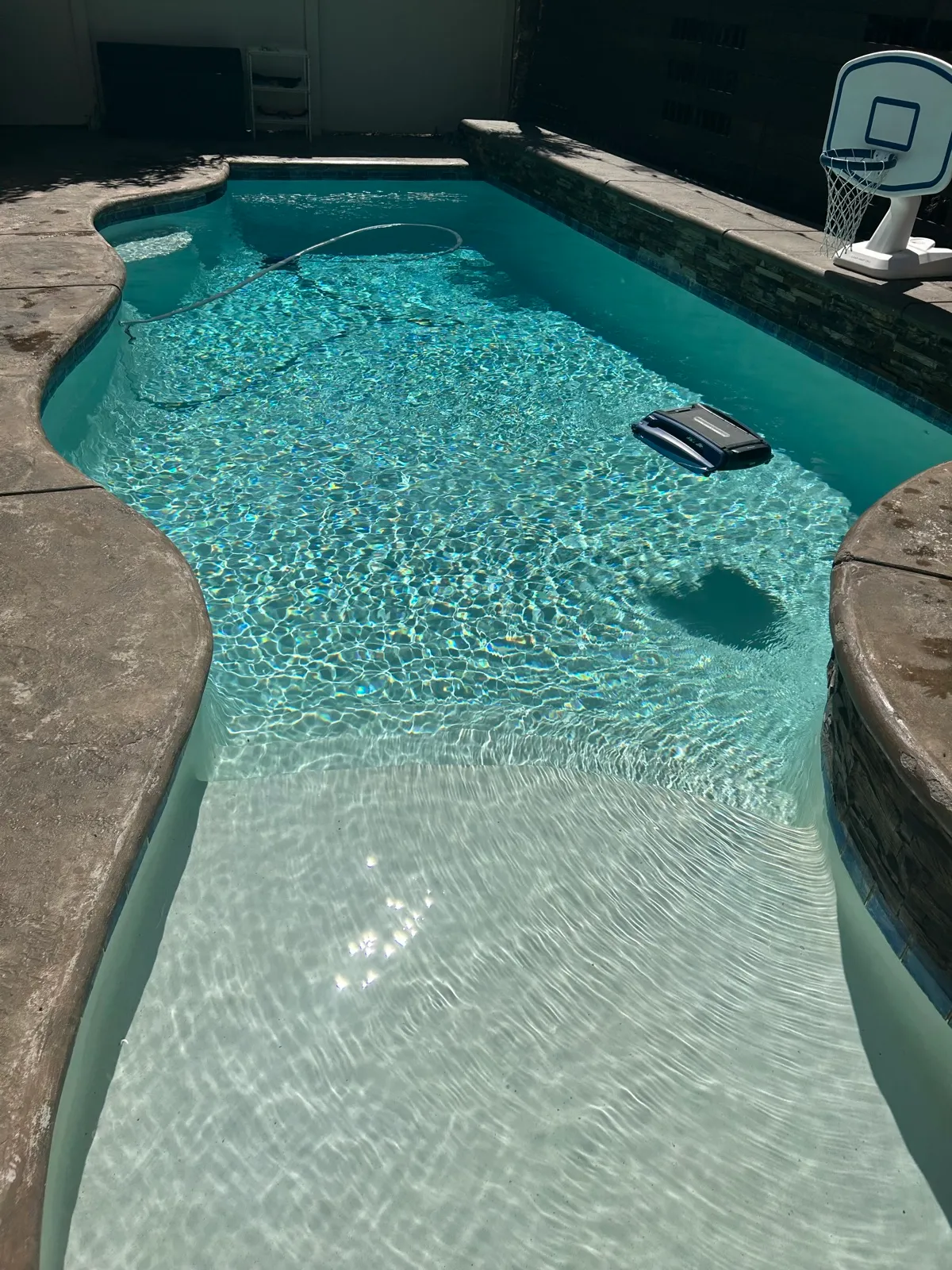 Overhead view of a freeform pool with rock waterfall feature and robotic cleaner working, crystal-clear water after professional pool service in Temescal Valley, CA