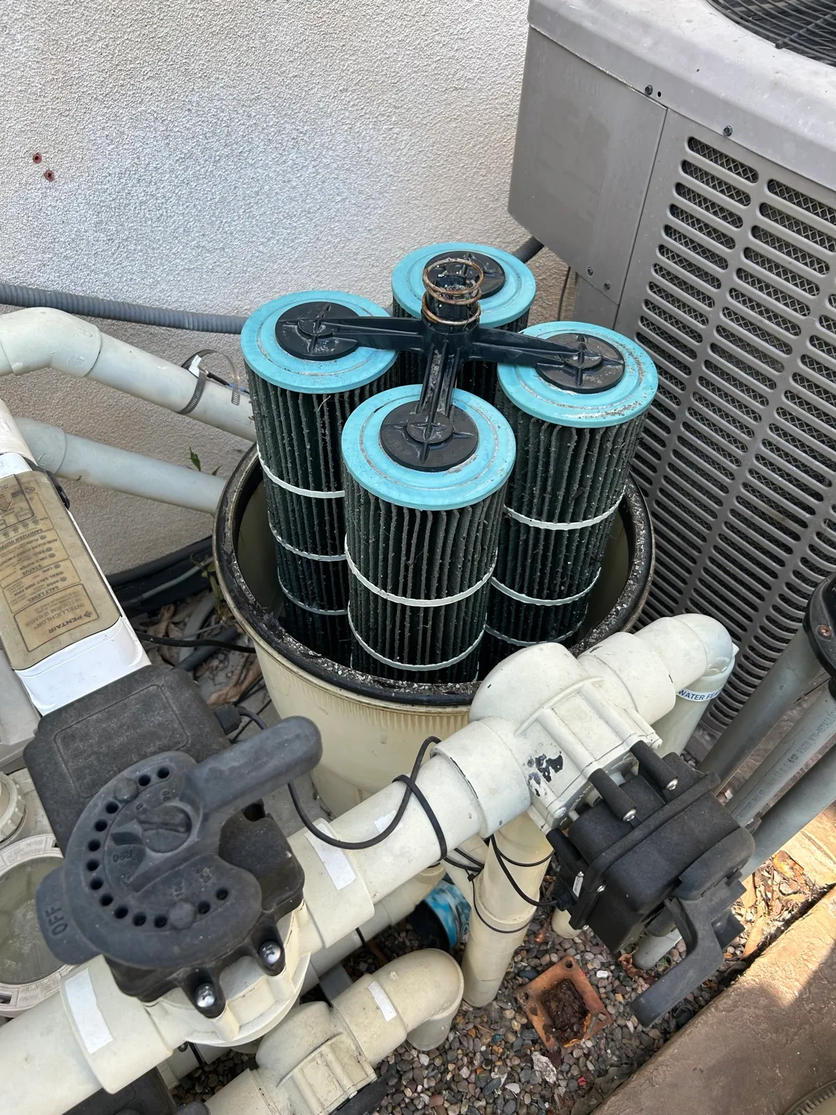 Dirty pool filter cartridge assembly removed from the housing for cleaning, showing four cartridge elements with accumulated debris during professional pool equipment maintenance