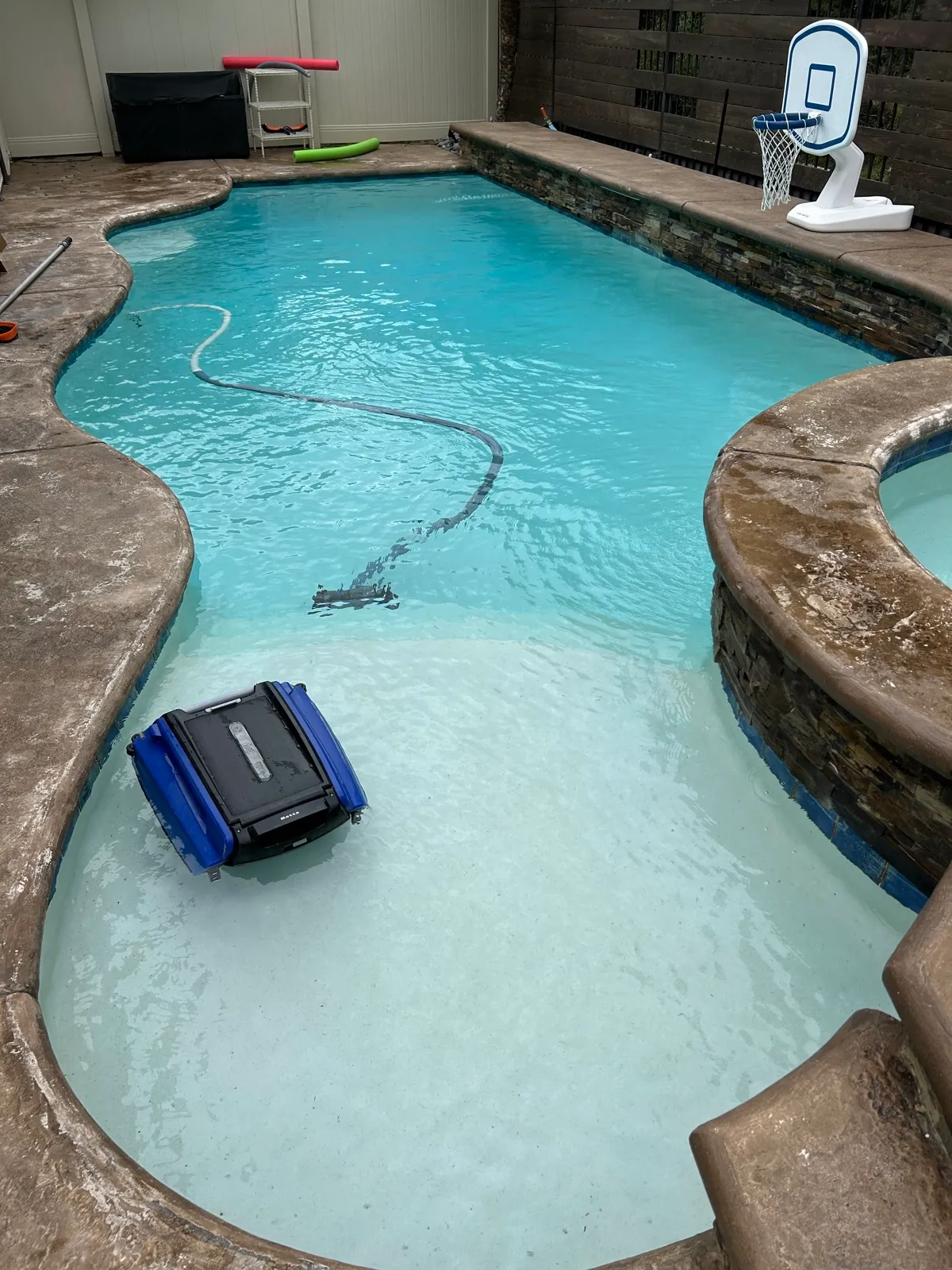 Robotic pool cleaner navigating the floor of a freeform backyard pool during a professional pool cleaning service visit in Temescal Valley, CA