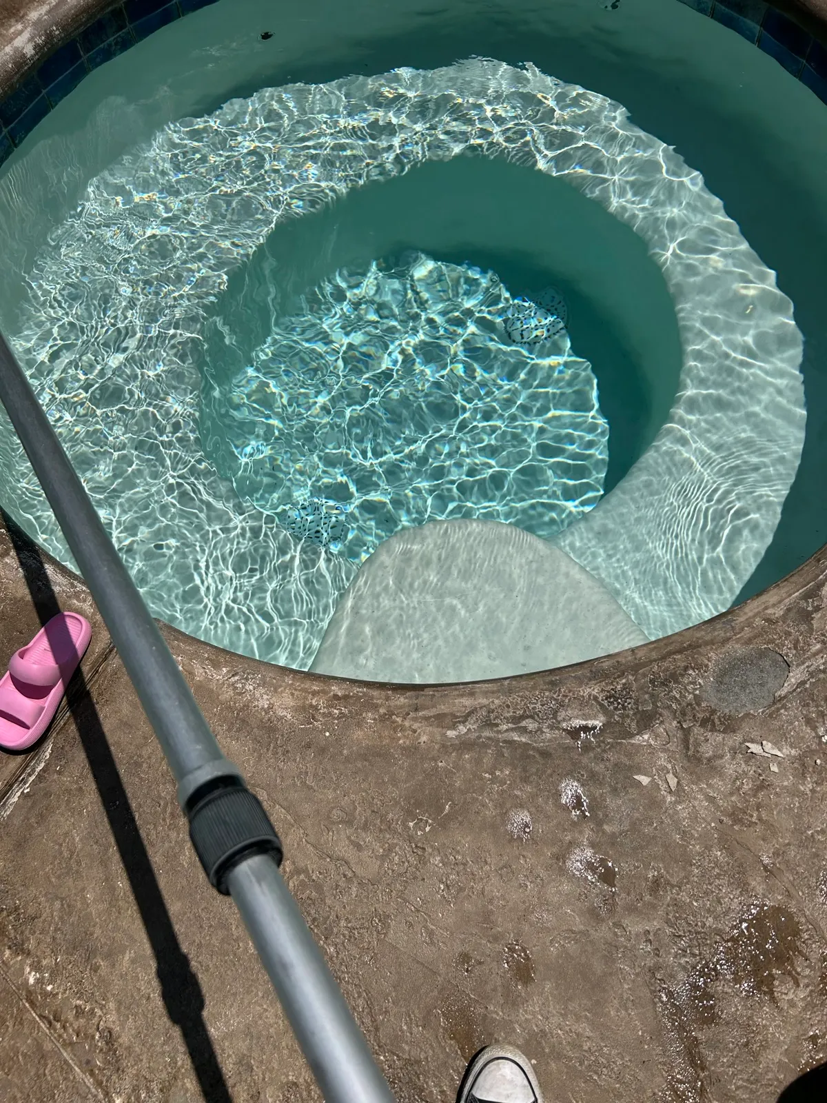 Round spa being cleaned with a brush attached to a telescoping pole during a professional pool and spa service visit in Temescal Valley, CA