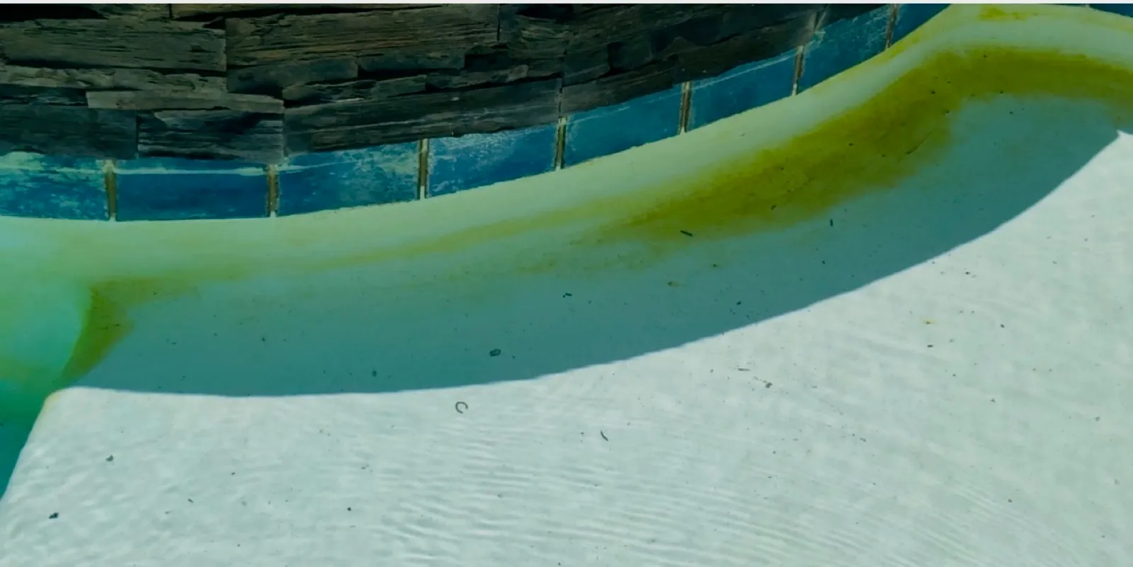 Underwater view of round spa entry steps coated in heavy green algae growth with tile line visible before professional pool and spa acid wash service in Temescal Valley